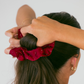 Person using a red scrunchie to tie their hair into a bun against a white background