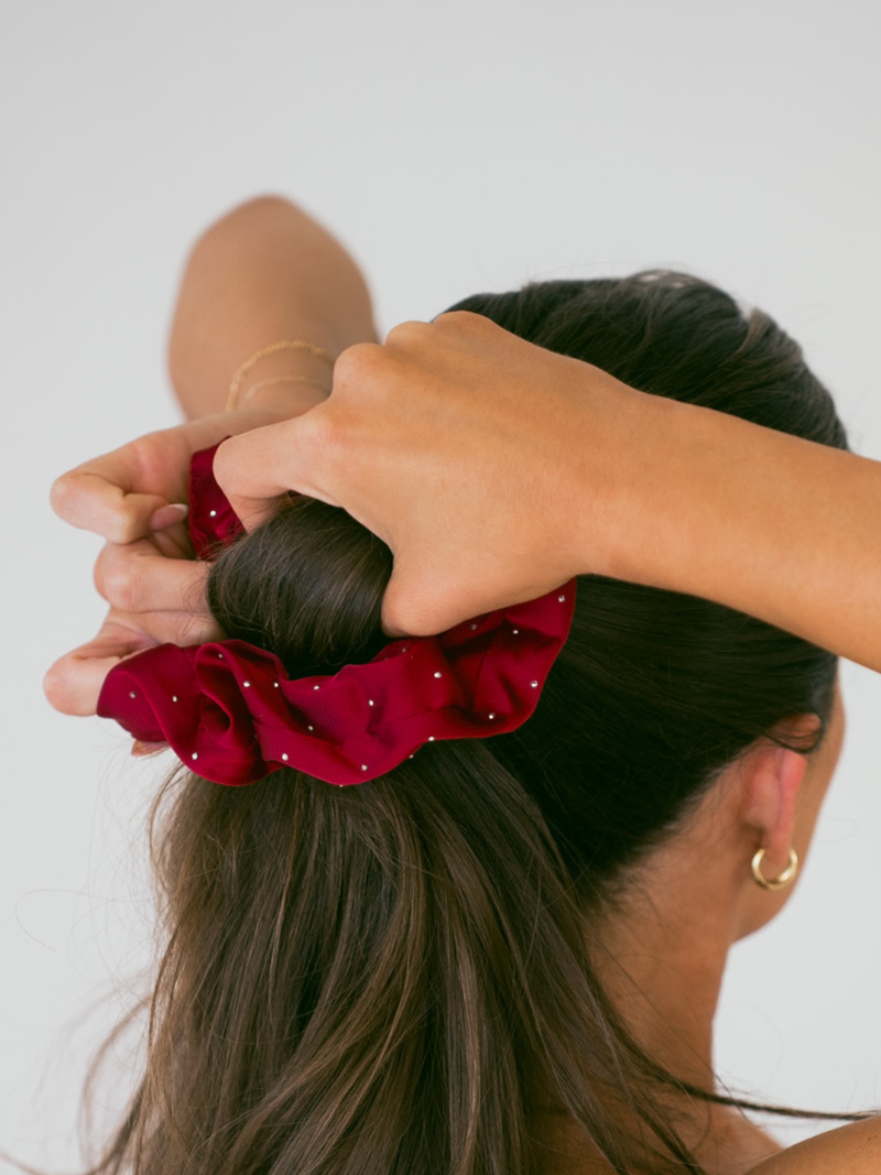 Person using a red scrunchie to tie their hair into a bun against a white background