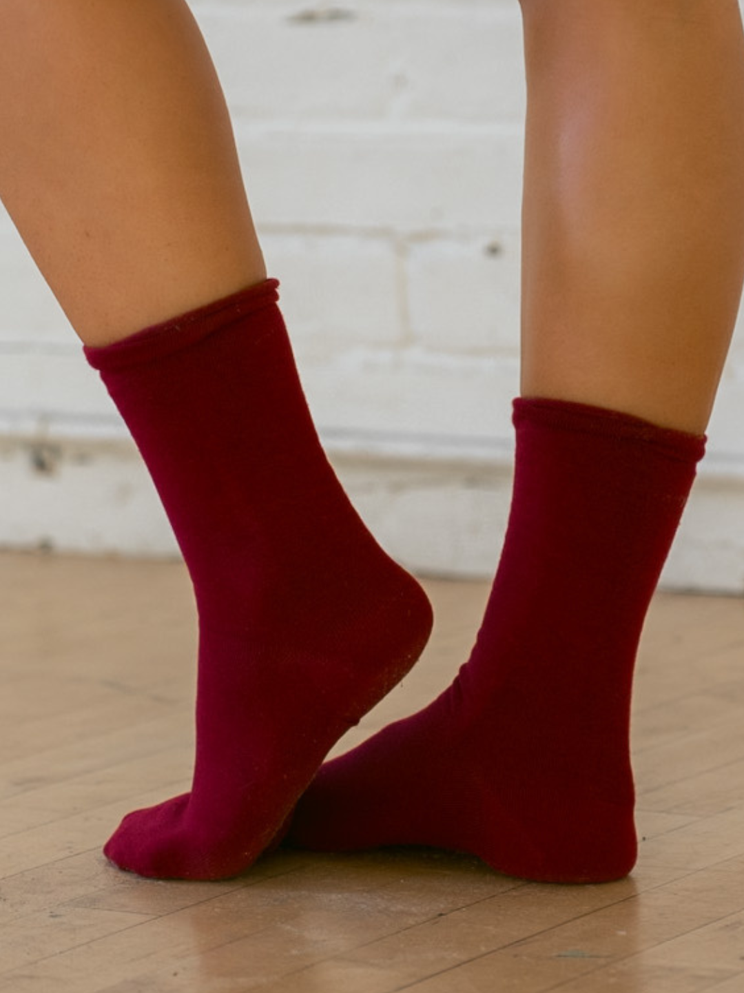 Red socks worn on a wooden floor with a white brick wall background
