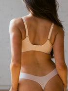 Woman wearing a beige bra and panties set against a neutral background