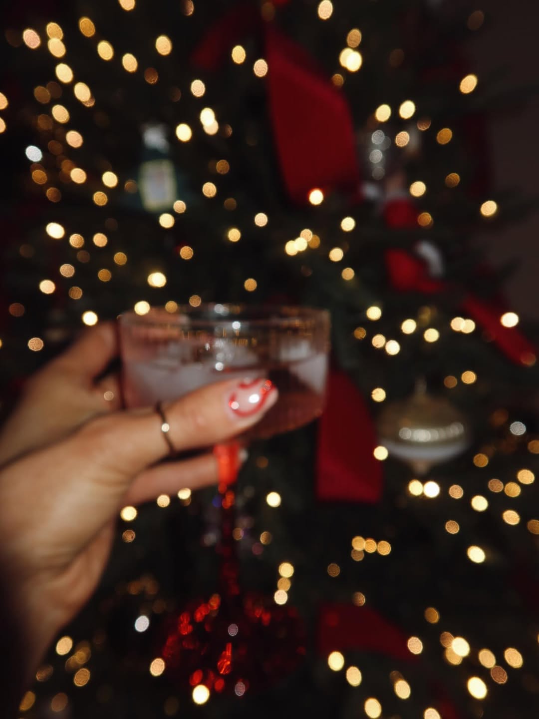Hand holding a glass of red wine with blurred lights in the background